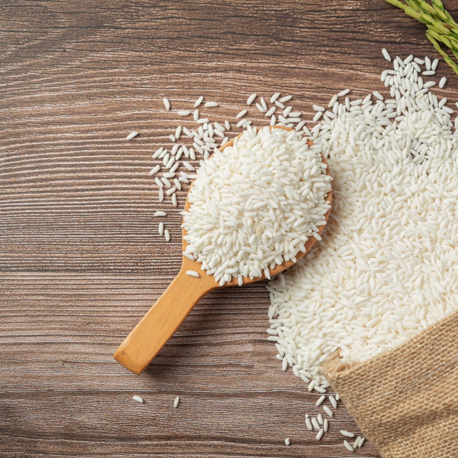 a sack of rice with rice on wooden spoon and rice plant